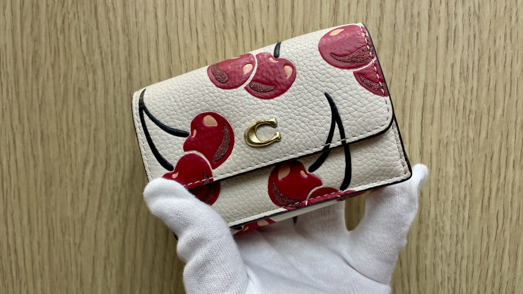COACH(コーチ)のエセンシャル・ミニ・トライフォールド・チェリー柄三つ折り財布(アイボリー)。Y2Kトレンドで人気が再爆発している、持っているだけでハッピーになる大人可愛いデザインです。